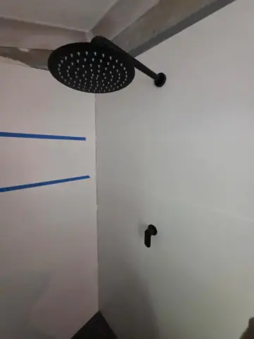 Shower rough-in with black rain head before tiling is finished