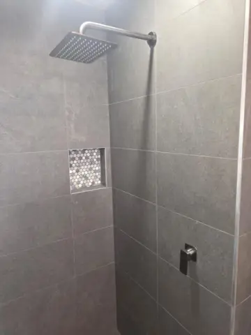 Square shower head and niche in a grey tiled shower