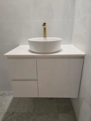 Round vessel basin with a gold mixer on a white vanity