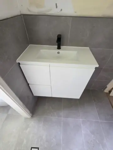 White vanity with black tapware on grey tiles